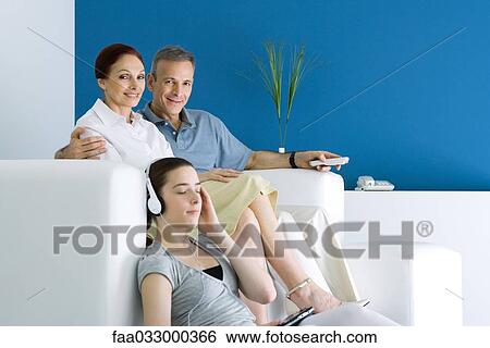Stock Photograph - Family together in living room, parents smiling at camera, teen girl listening to headphones. Fotosearch
