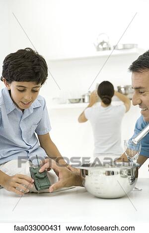 Father and son in kitchen, looking at toy tank together, woman in background View Large Photo Image Stock Image - Father and son in kitchen, looking at toy tank together, woman in background. Fotosearch