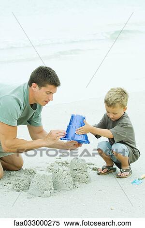 Father and son playing with sand bucket at the beach, looking down View Large Photo Image Stock Photography - Father and son playing with sand bucket at the beach, looking down. Fotosearch