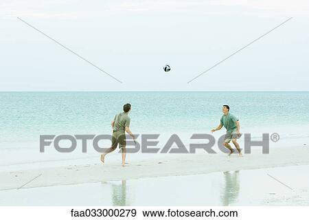 Stock Photo - Father and teen son at the beach, both looking up at ball in midair. Fotosearch