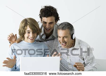Stock Photograph - Father and two sons looking at laptop computer together, smiling, hands raised. Fotosearch