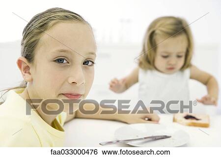 Girl sitting at table with younger sister, smiling over shoulder at camera View Large Photo Image Stock Photograph - Girl sitting at table with younger sister, smiling over shoulder at camera. Fotosearch