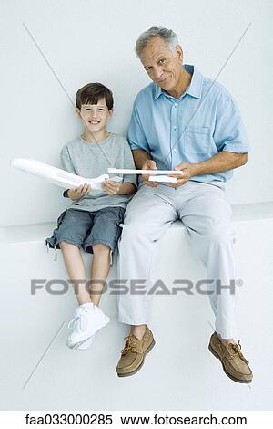 Grandfather and grandson sitting side by side, holding model airplane pieces, smiling at camera View Large Photo Image Stock Photography - Grandfather and grandson sitting side by side, holding model airplane pieces, smiling at camera. Fotosearch