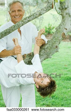 Stock Image - Grandfather holding up grandson hanging from tree, both smiling at camera. Fotosearch