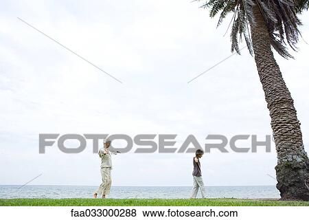Stock Photo - Grandmother and grandson walking at seashore, arms out, side view. Fotosearch