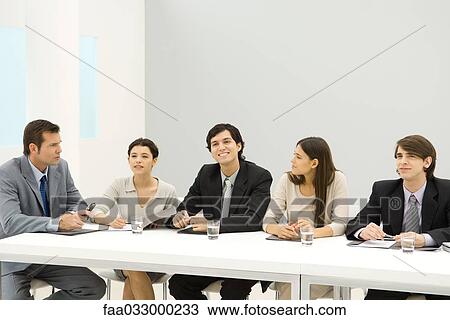 Group of business associates sitting at conference table, looking away, smiling View Large Photo Image Stock Image - Group of business associates sitting at conference table, looking away, smiling. Fotosearch