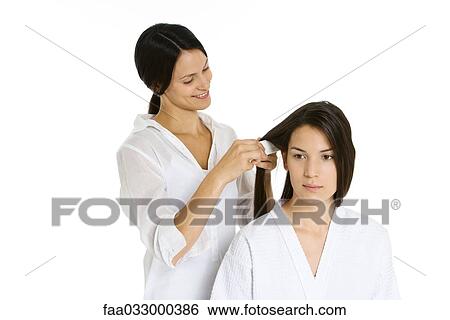 Stock Photograph - Hair stylist combing woman's hair, both looking away. Fotosearch