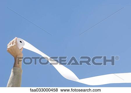 Stock Photo - Hand holding roll of paper in front of blue sky. Fotosearch
