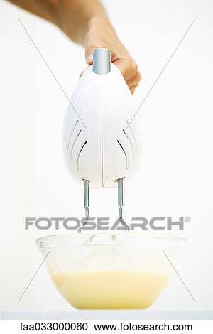 Stock Image - Hand using electric mixer in bowl of batter, close-up, low angle view. Fotosearch