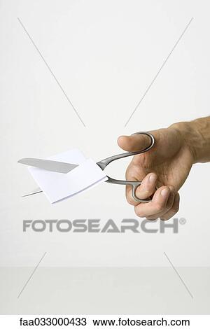 Stock Image - Hand using scissors to cut paper. Fotosearch