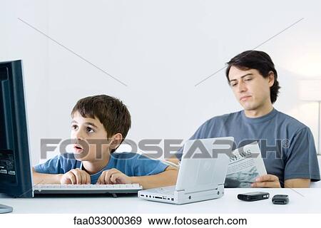 Stock Photo - Little boy computer and portable DVD player, father reading newspaper in background. Fotosearch