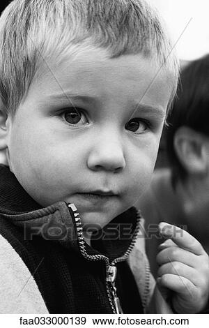 Stock Photo - Little boy looking at camera, pointing at his mouth, portrait. Fotosearch