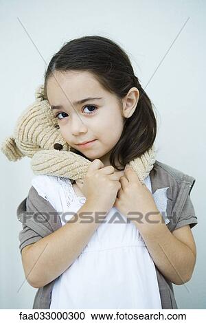 Stock Image - Little girl with teddy bear hanging around her neck, smiling at camera, portrait. Fotosearch