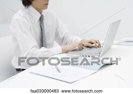 Stock Image - Male sitting at desk using laptop, cropped view. Fotosearch