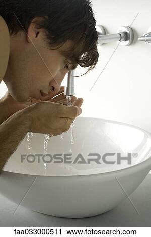 Stock Image - Man bending over sink, splashing water on face, cropped. Fotosearch