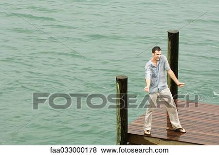 Stock Photo - Man dancing on dock, getting wet, arms out, high angle view. Fotosearch