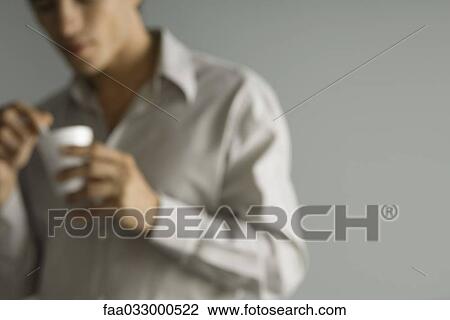 Stock Image - Man holding disposable coffee cup, defocused, cropped. Fotosearch