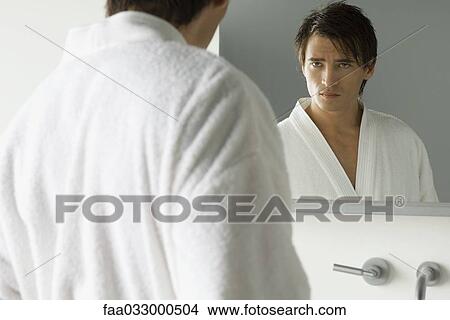 Picture - Man looking at himself in mirror, wearing bathrobe, furrowing brow. Fotosearch