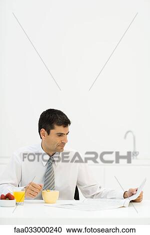 Stock Image - Man sitting at breakfast table, reading newspaper. Fotosearch