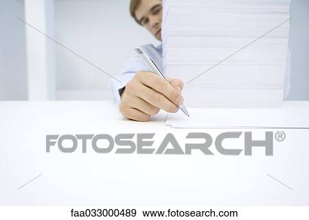 Stock Photo - Man sitting behind tall stack of documents, writing on single sheet of paper. Fotosearch