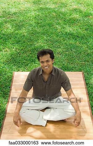 Man sitting cross-legged outdoors, smiling at camera, high angle view View Large Photo Image Stock Image - Man sitting cross-legged outdoors, smiling at camera, high angle view. Fotosearch