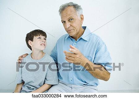 Picture - Man sitting with arm around grandson's shoulders, man looking at camera. Fotosearch