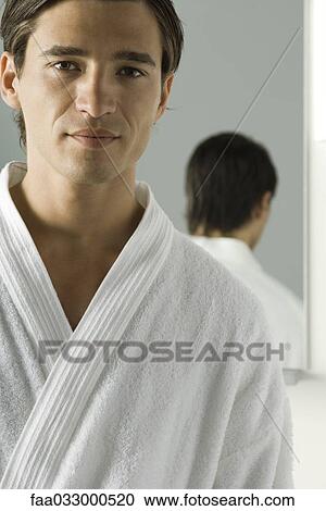 Stock Image - Man wearing bathrobe, smiling at camera, mirror in background. Fotosearch