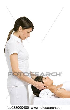 Stock Image - Massage therapist performing head massage, side view. Fotosearch