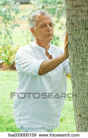 Mature man touching tree trunk, eyes closed View Large Photo Image Stock Photo - Mature man touching tree trunk, eyes closed. Fotosearch