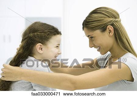 Stock Image - Mother and daughter face to face, smiling, woman touching girl's hair. Fotosearch