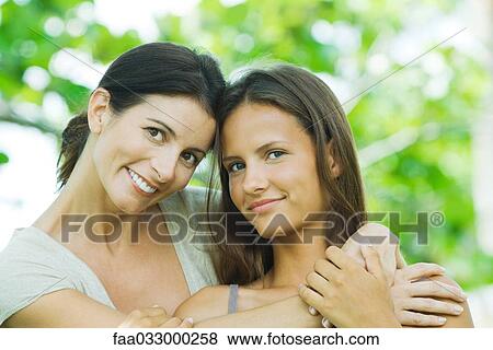 Stock Photo - Mother embracing teen daughter, both smiling at camera, portrait. Fotosearch