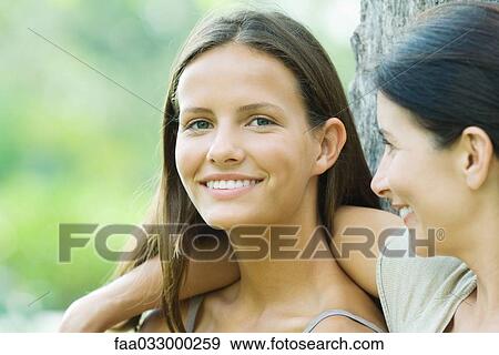 Stock Photo - Mother looking at teen daughter, daughter smiling at camera. Fotosearch