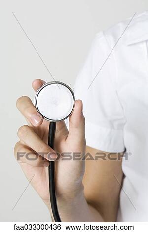 Stock Photograph - Nurse holding stethoscope, cropped view of hand. Fotosearch
