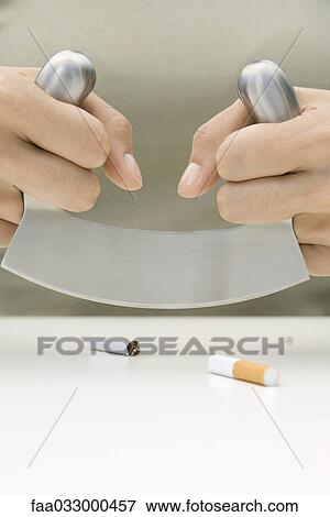Stock Photo - Person cutting cigarette in half with meat cleaver, cropped view of hands. Fotosearch