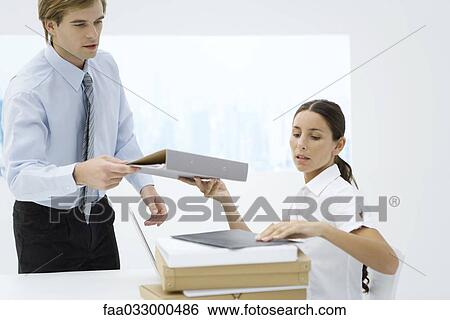 Stock Photograph - Professional woman handing binder to colleague from stack of many binders. Fotosearch