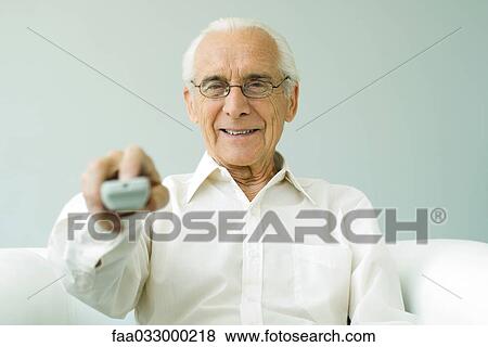 Stock Photo - Senior man pointing remote control at camera, smiling. Fotosearch