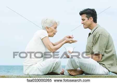 Stock Photography - Senior woman and adult son sitting face to face, sharing take out food, side view. Fotosearch