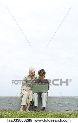 Senior woman and grandson sitting outdoors, using laptop computer together View Large Photo Image Stock Photo - Senior woman and grandson sitting outdoors, using laptop computer together. Fotosearch