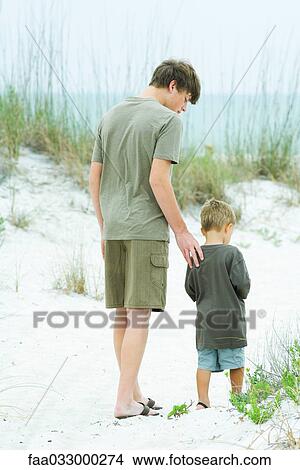 Teen boy walking with little brother at the beach, rear view View Large Photo Image Picture - Teen boy walking with little brother at the beach, rear view. Fotosearch