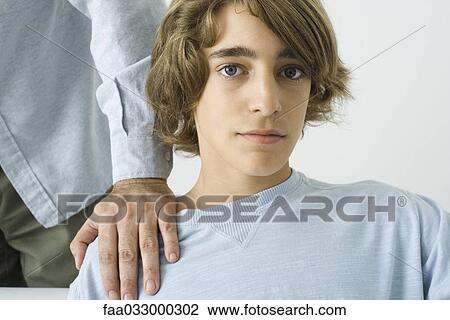 Stock Image - Teen boy with man's hand on his shoulder, looking at camera. Fotosearch