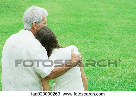Stock Image - Teen girl leaning head on grandfather's shoulder, rear view. Fotosearch