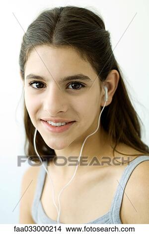 Picture - Teen girl listening to earphones, smiling at camera. Fotosearch