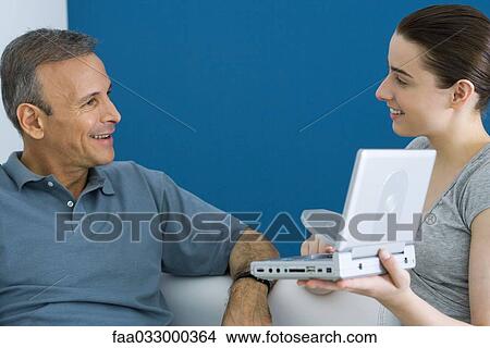 Picture - Teen girl showing her father portable DVD player, both smiling. Fotosearch