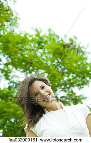 Stock Image - Teen girl smiling outdoors, hair tousled by breeze, low angle view. Fotosearch