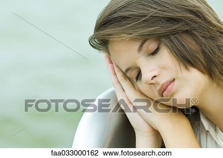 Stock Image - Teenage girl resting head on clasped hands, eyes closed, close-up. Fotosearch