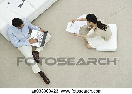 Stock Image - Two colleagues sitting on the ground, discussing document, overhead view. Fotosearch