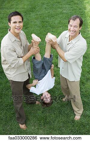 Two men holding little boy upside down by his legs, all smiling, high angle view View Large Photo Image Stock Photograph - Two men holding little boy upside down by his legs, all smiling, high angle view. Fotosearch