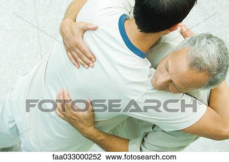 Stock Image - Two men hugging, high angle view. Fotosearch