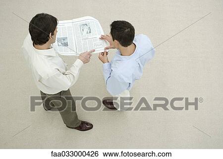 Stock Photograph - Two men looking at newspaper together, overhead view. Fotosearch