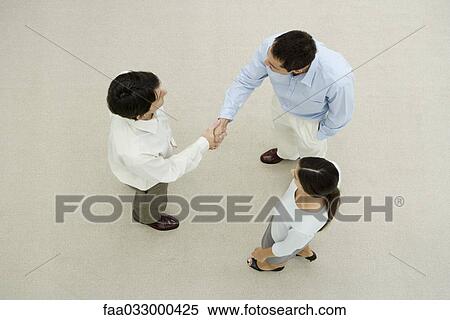 Two men shaking hands, female colleague watching, overhead view View Large Photo Image Stock Photography - Two men shaking hands, female colleague watching, overhead view. Fotosearch